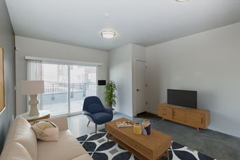 A living room with a white couch, a blue chair, a wooden coffee table, and a flat screen tv.
